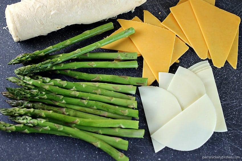 Cheesy Asparagus Puffs are a quick appetizer or side dish. Fresh asparagus wrapped up with provolone and cheddar cheeses and baked in a crescent roll - easy, cheesy, and delicious! | www.persnicketyplates.com #cheese #cheesy #appetizer #asparagus #vegetarian fresh asparagus laid out with sliced cheese for asparagus puffs