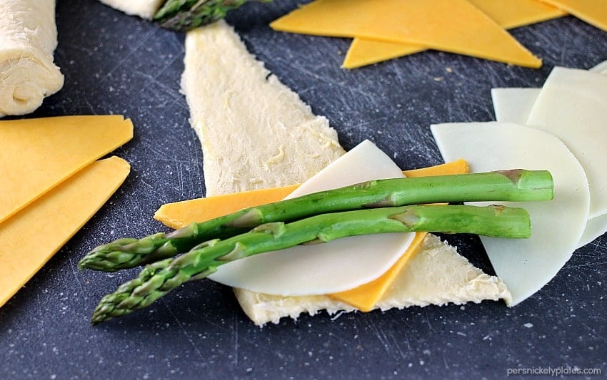 Cheesy Asparagus Puffs are a quick appetizer or side dish. Fresh asparagus wrapped up with provolone and cheddar cheeses and baked in a crescent roll - easy, cheesy, and delicious! | www.persnicketyplates.com #cheese #cheesy #appetizer #asparagus #vegetarian cheesy asparagus puffs prepped on a cutting board