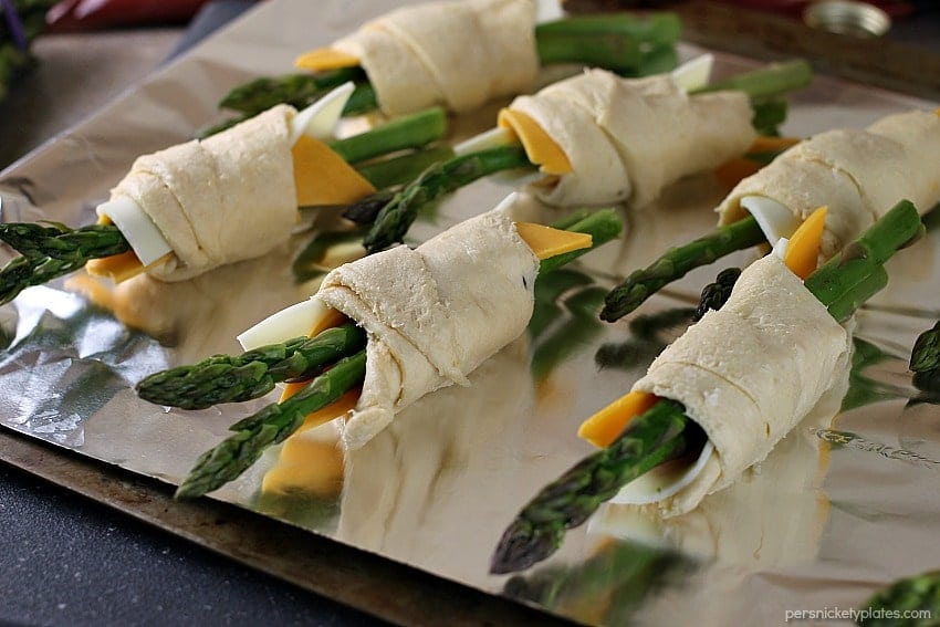 Cheesy Asparagus Puffs are a quick appetizer or side dish. Fresh asparagus wrapped up with provolone and cheddar cheeses and baked in a crescent roll - easy, cheesy, and delicious! | www.persnicketyplates.com #cheese #cheesy #appetizer #asparagus #vegetarian asparagus puffs prepped on a baking sheet ready for the oven