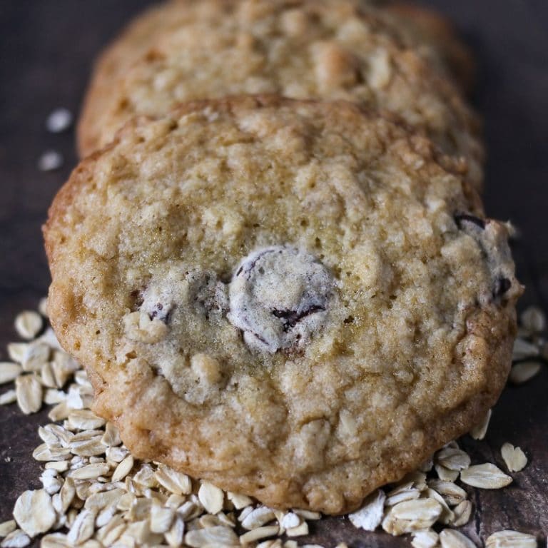 three ranger cookies on a dark wood table and spilled oats