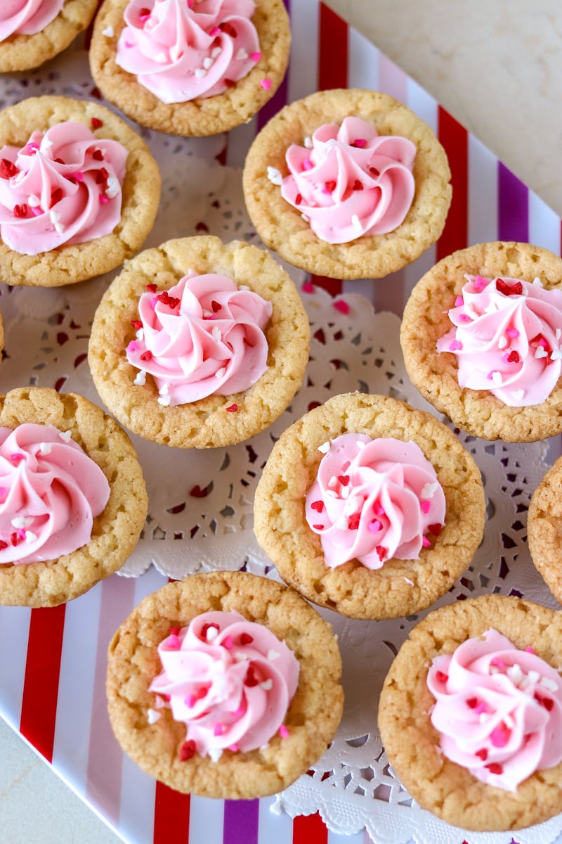 plate of valentine sugar cookie cups with pink frosting & heart sprinkles Valentine Sugar Cookie Cups are a simple, semi-homemade treat that you can whip up in no time! A sugar cookie base filled with pink frosting and topped with Valentine sprinkles. | www.persnicketyplates.com