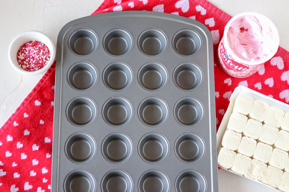 mini muffin pan and supplies for valentine sugar cookie cups Valentine Sugar Cookie Cups are a simple, semi-homemade treat that you can whip up in no time! A sugar cookie base filled with pink frosting and topped with Valentine sprinkles. | www.persnicketyplates.com