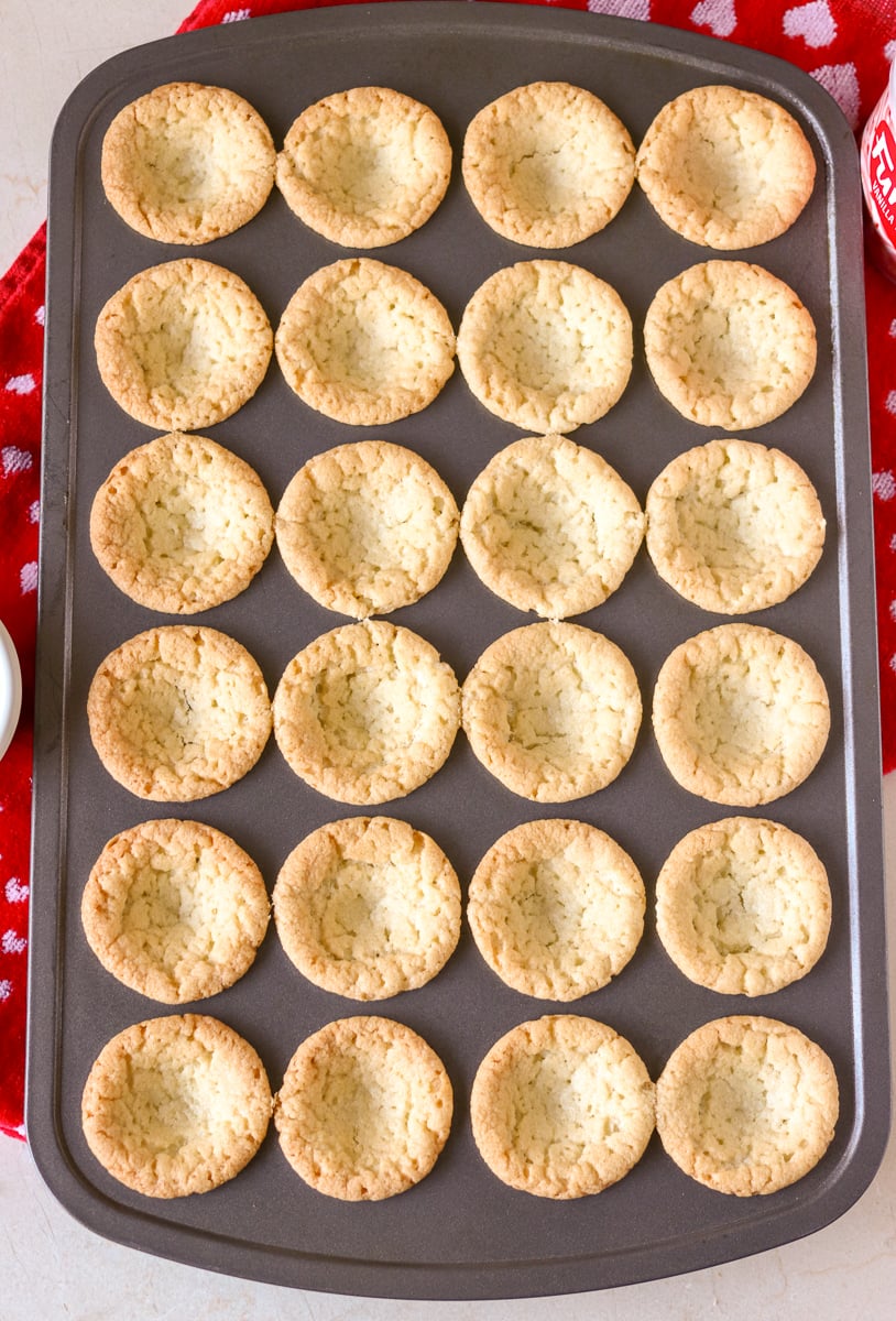 pan of 24 sugar cookie cups fresh out of the oven Valentine Sugar Cookie Cups are a simple, semi-homemade treat that you can whip up in no time! A sugar cookie base filled with pink frosting and topped with Valentine sprinkles. | www.persnicketyplates.com