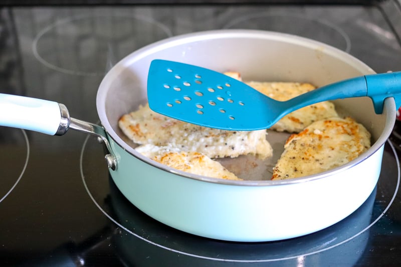 skillet with chicken breasts on stove with spatula