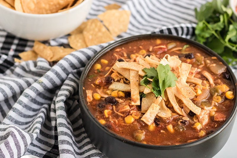 black bowl of chicken tortilla soup with a dish towel