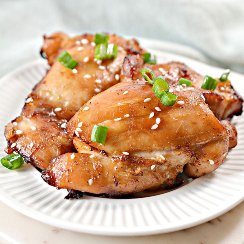 air fried sticky chicken thighs on a white plate with green onion & sesame seed garnish