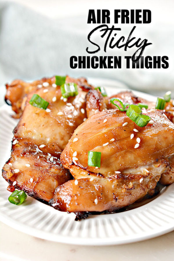 air fried sticky chicken thighs on a white plate with green onion & sesame seed garnish