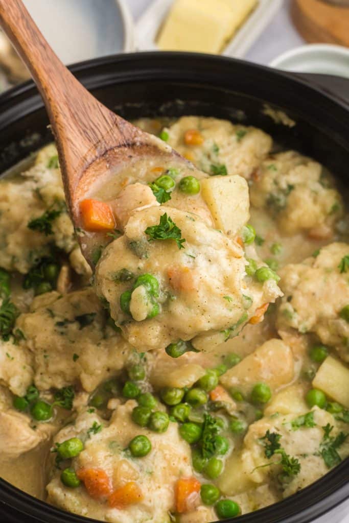 wooden spoon scooping chicken and dumplings from a pot.