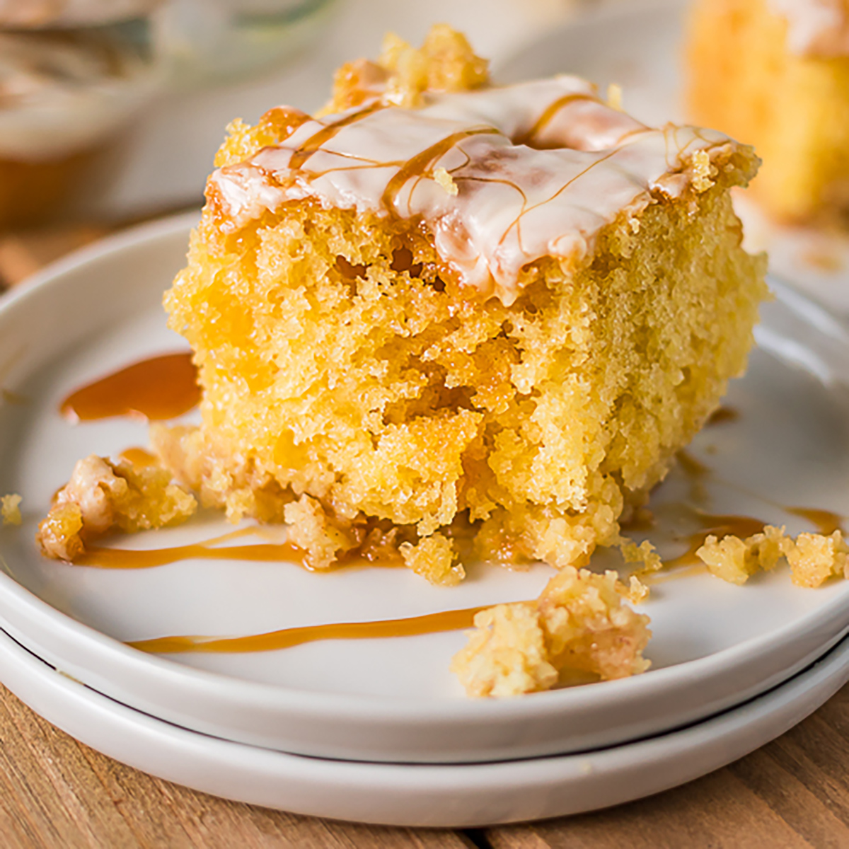 slice of caramel apple poke cake on white plates drizzled with caramel