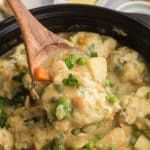 wooden spoon lifting a scoop of chicken and dumplings out of a pot.