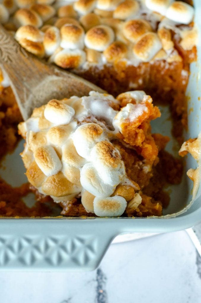 scoop of marshmallow topped sweet potato casserole on wooden spoon