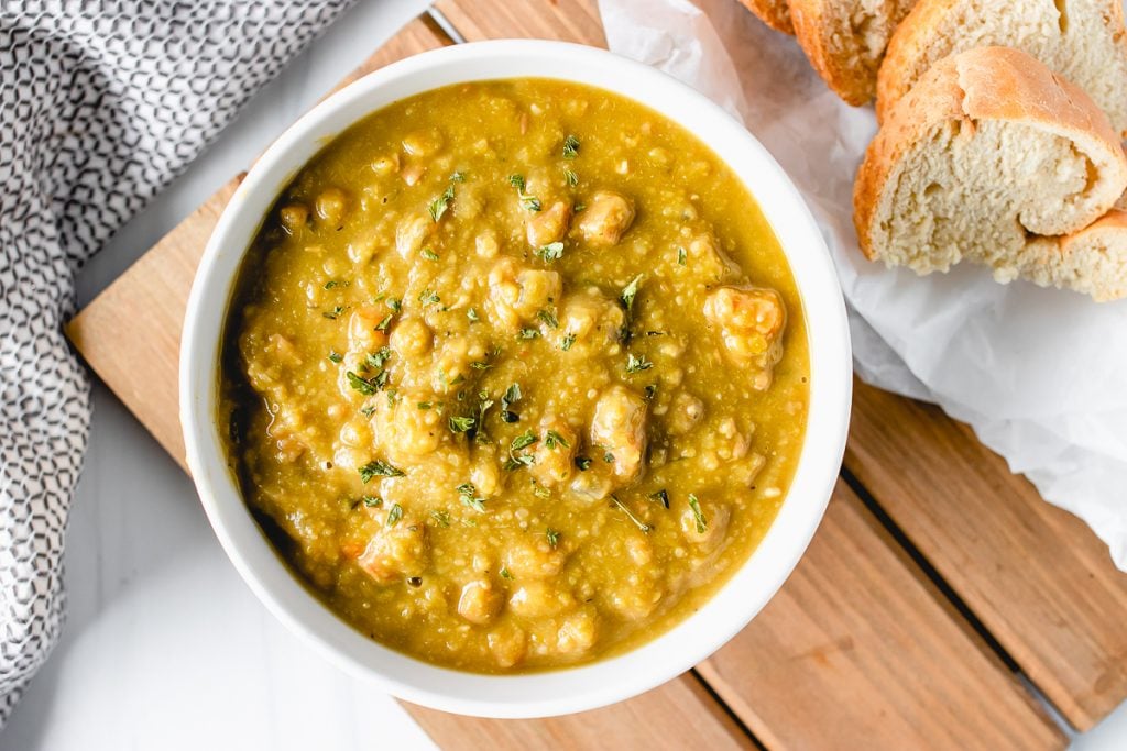 bowl of split pea soup next to a chunk of french bread