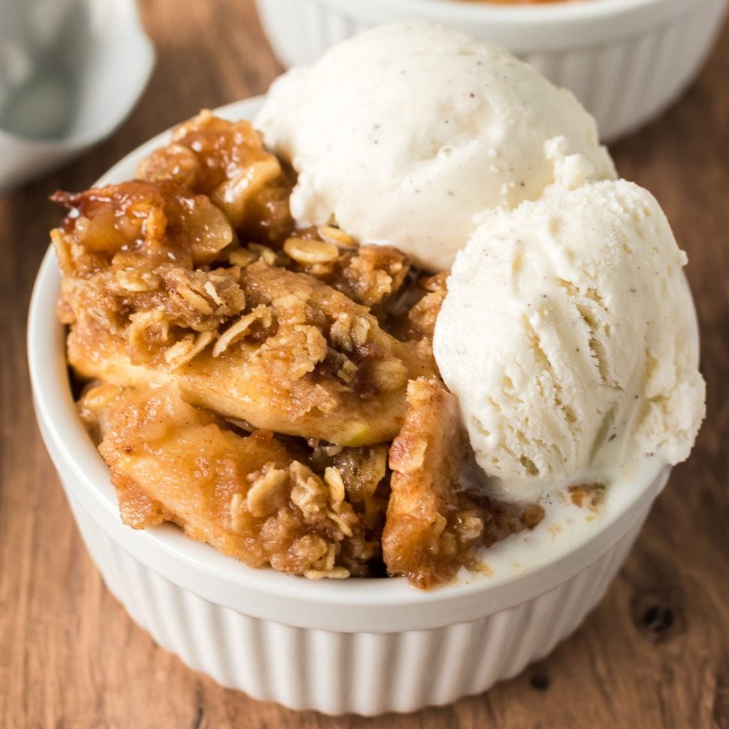 apple crisp topped with vanilla ice cream in a white bowl