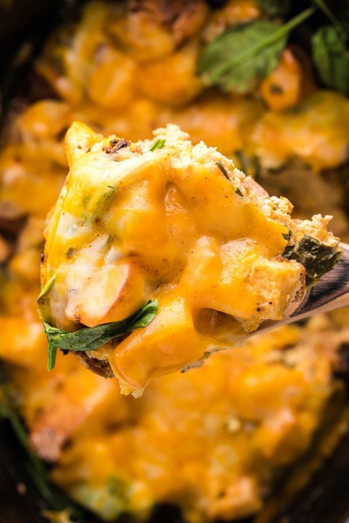 scoop of eggs benedict casserole being lifted from a crockpot