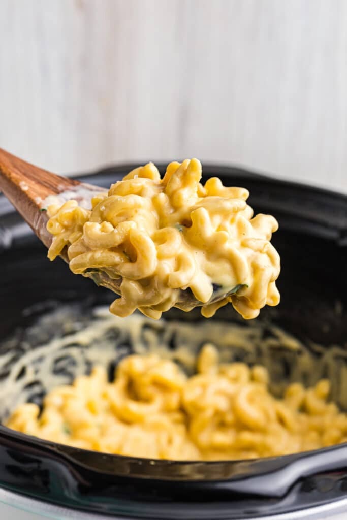 spoon lifting a scoop of mac & cheese from a crockpot.