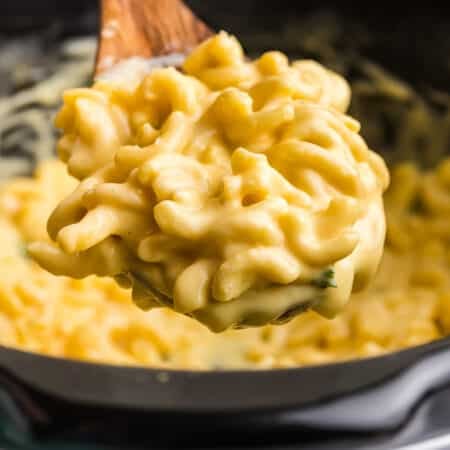 spoon lifting a scoop of mac & cheese from a slow cooker.