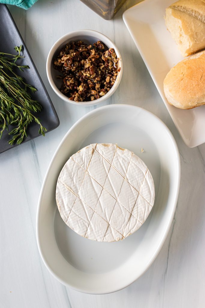 brie in a baking dish, scored & ready to be topped for baking