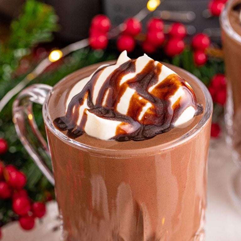 hot chocolate in a glass mug topped with whipped cream and chocolate sauce