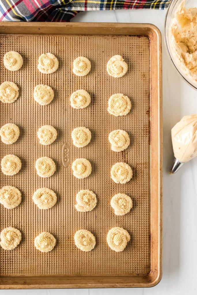 overhead shot of dough piped onto a baking sheet next to a pastry bag