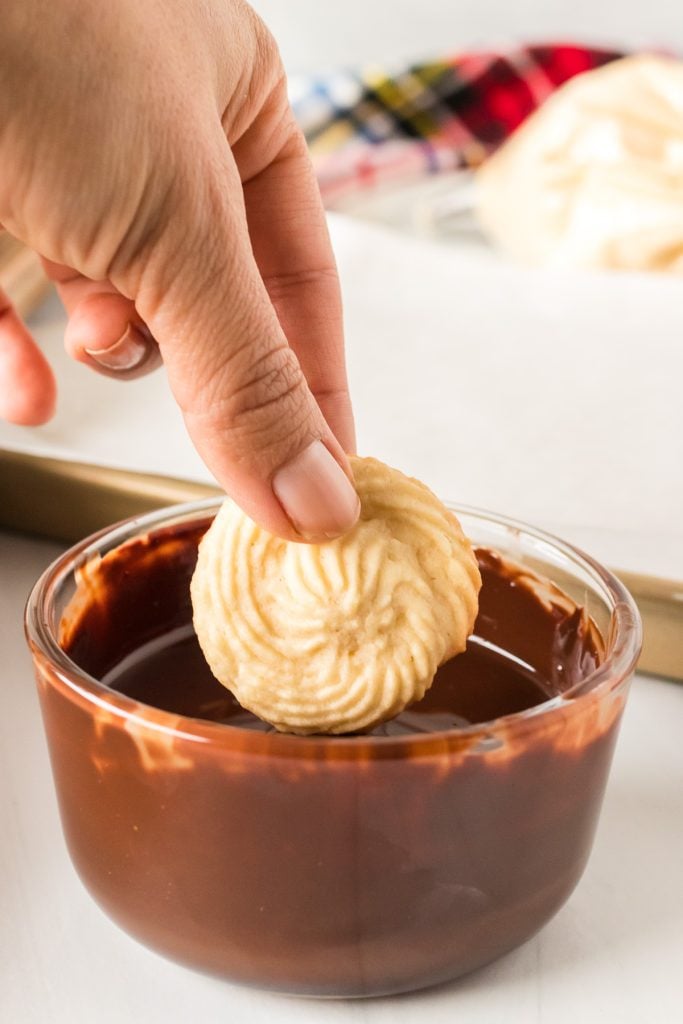 a hand dipping a butter cookie into melted chocolate