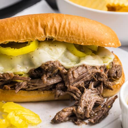 Italian beef sandwich with melted cheese and peppers served next to a bowl of chips.