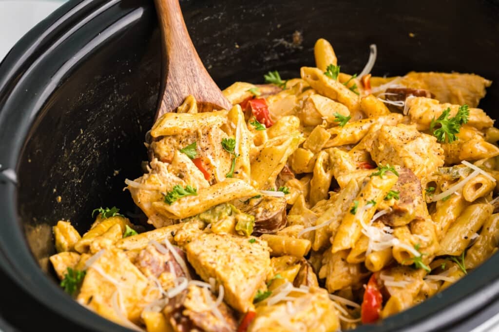 closeup of cajun chicken alfredo in a slow cooker with a wooden spoon.