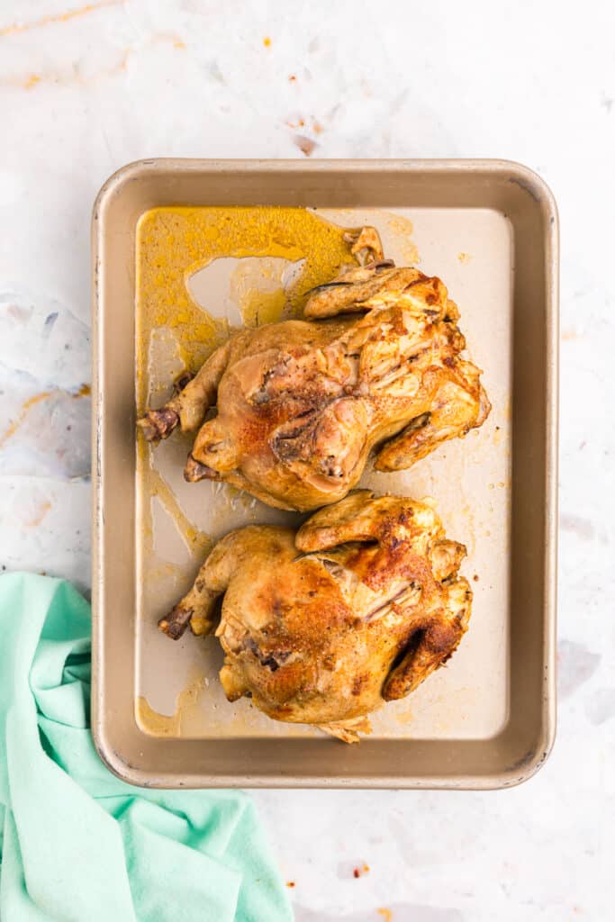 Cooked Cornish hens resting on a tray after broiling.