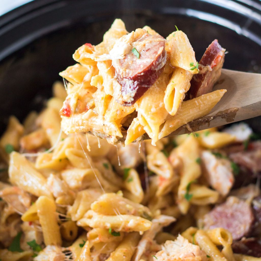 wooden spoon scooping cajun chicken pasta from a slow cooker.