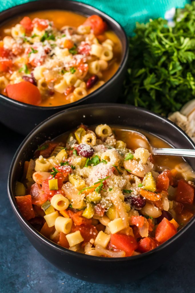 two bowls of minestrone soup in black bowls.