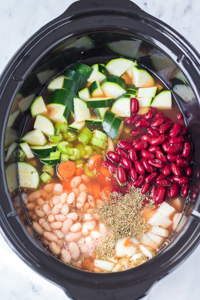 overhead shot of ingredients in slow cooker making minestrone soup.