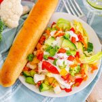 overhead shot of a vegetable chopped salad with a breadstick in a bowl.