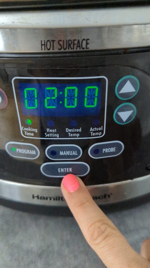 finger pressing the controls of a hamilton beach digital slow cooker.