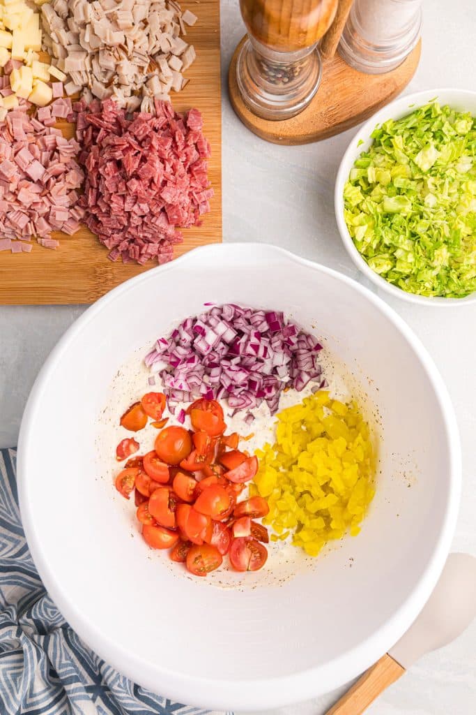 overhead shot of diced onion, banana peppers, and tomatoes in a white bowl.