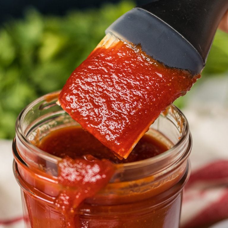 basting brush dipping into jar of honey bbq sauce.