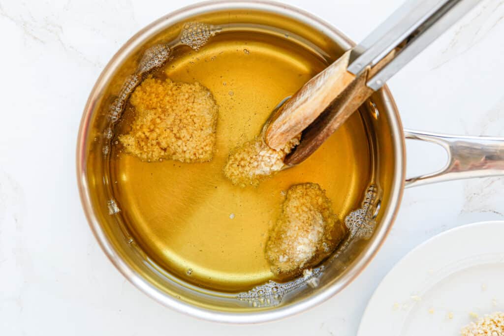 tongs turning chicken in oil.