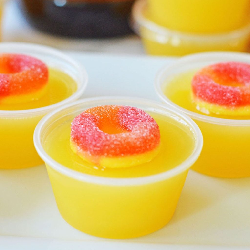 closeup of a fuzzy navel jello shot topped with a peach ring candy.