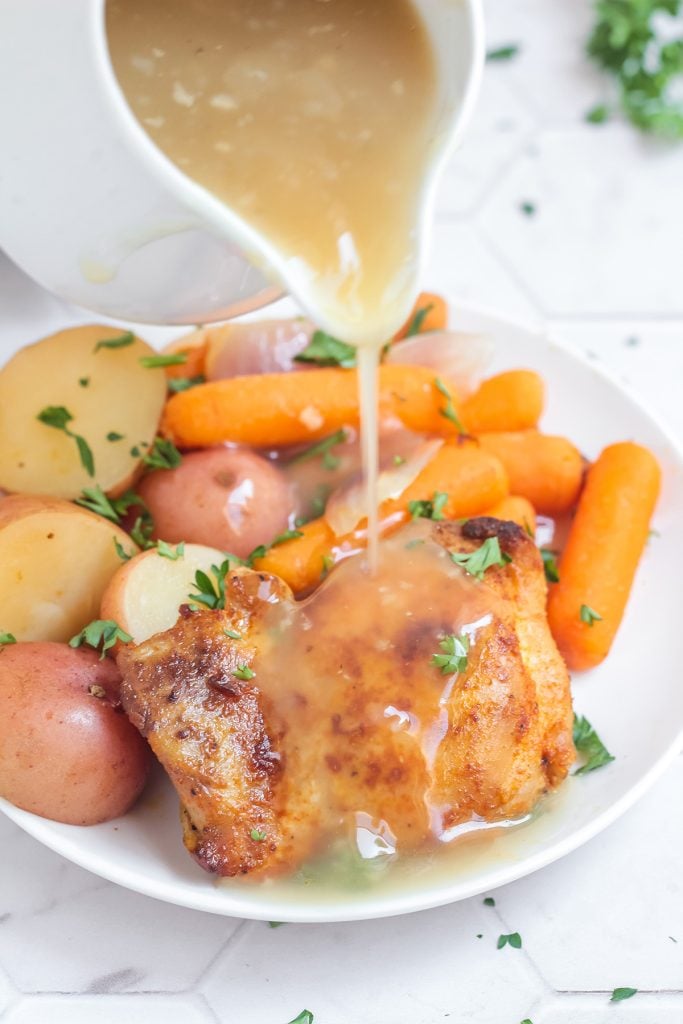 gravy pouring over chicken thighs, potatoes, & carrots.