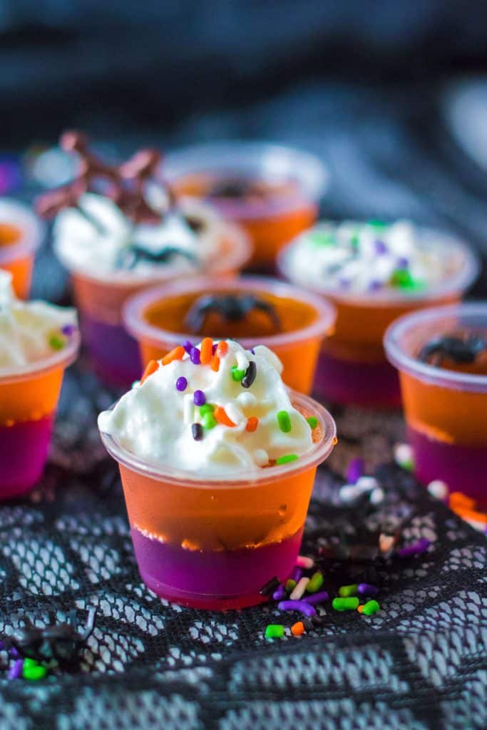 several orange and purple jello shots on a black web cloth.