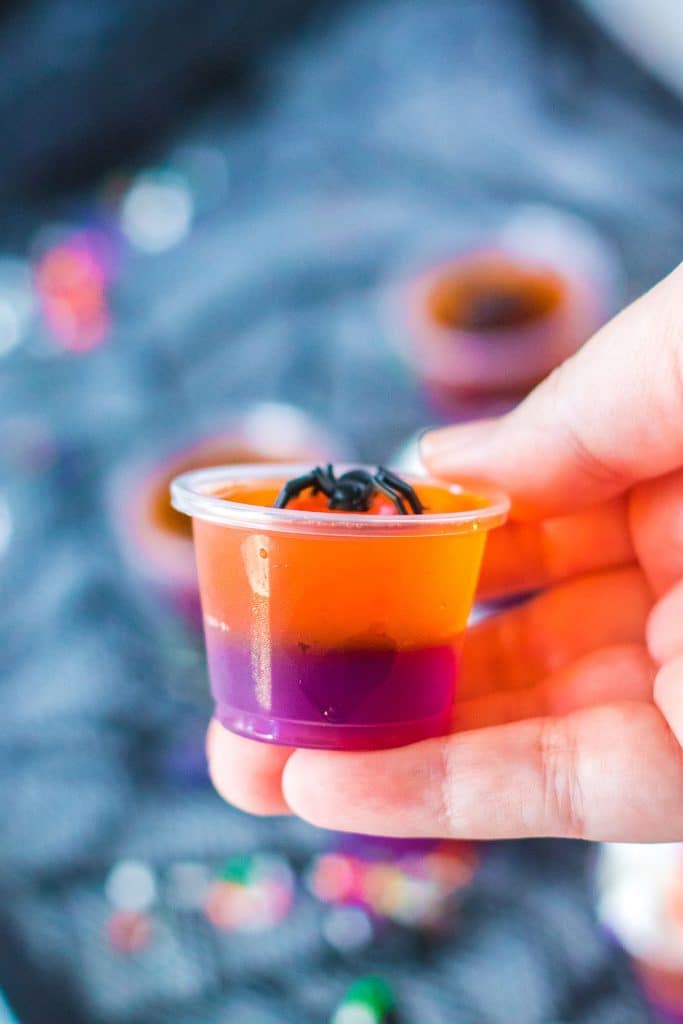 hand holding a halloween jello shot topped with a plastic spider.