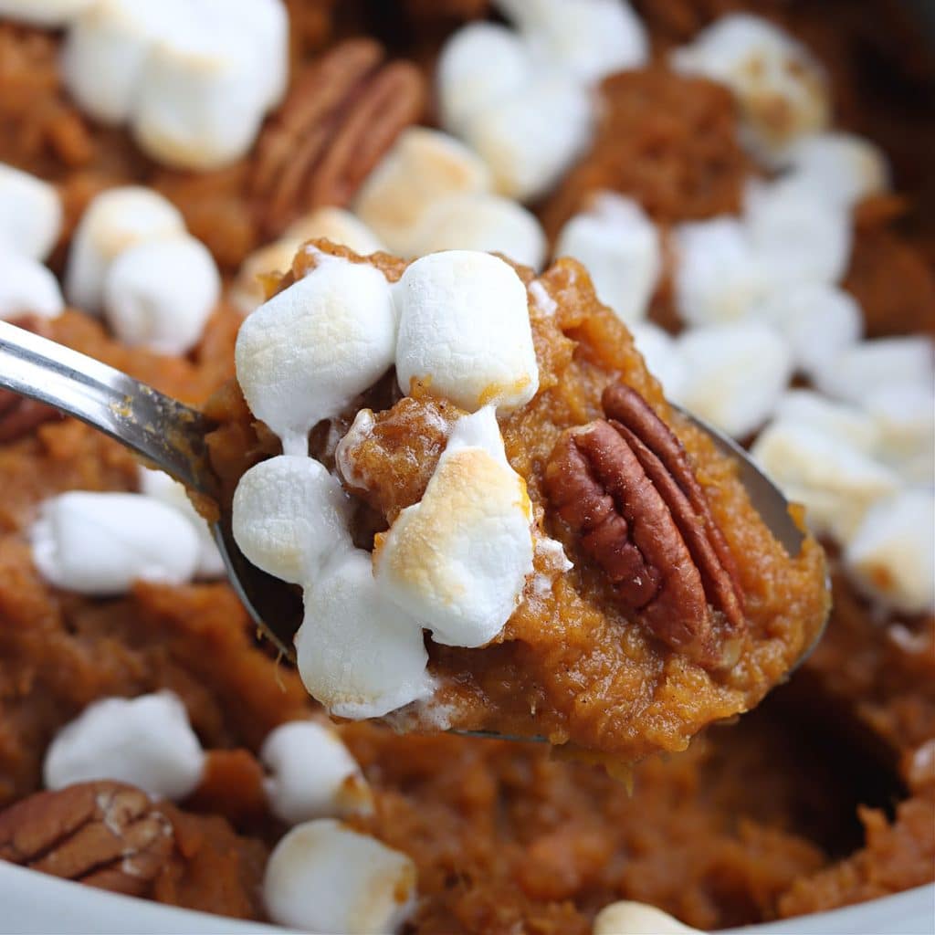 spoon scooping sweet potato casserole from a slow cooker.