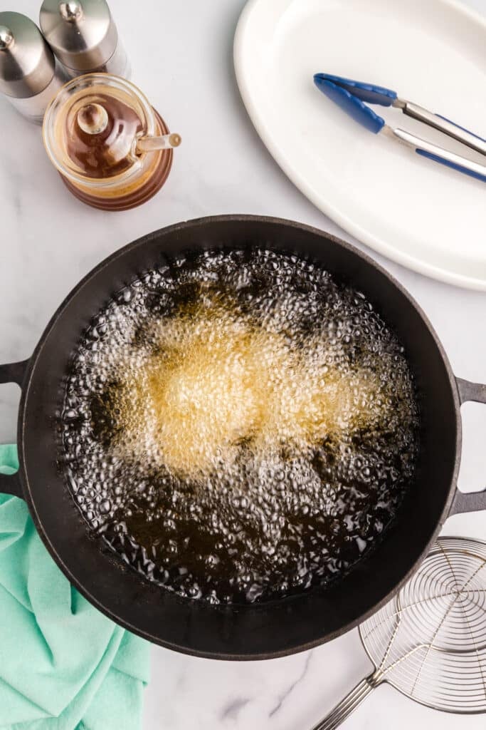 Chicken nuggets frying in bubbling oil in a cast iron pan.