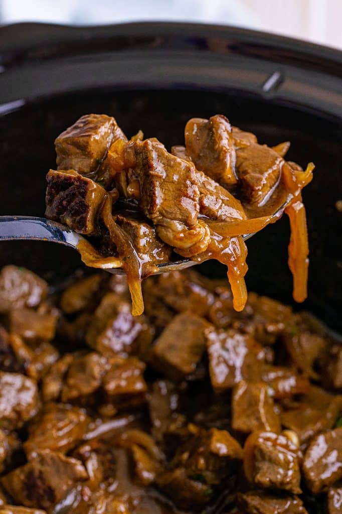spoon scooping steak bites from a crockpot.