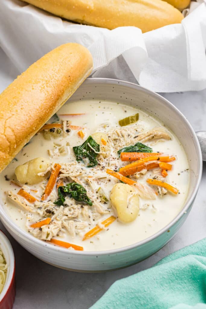 bowl of chicken gnocchi soup with a breadstick resting on the edge.