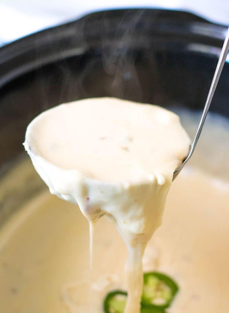 ladle scooping hot queso from a crockpot.
