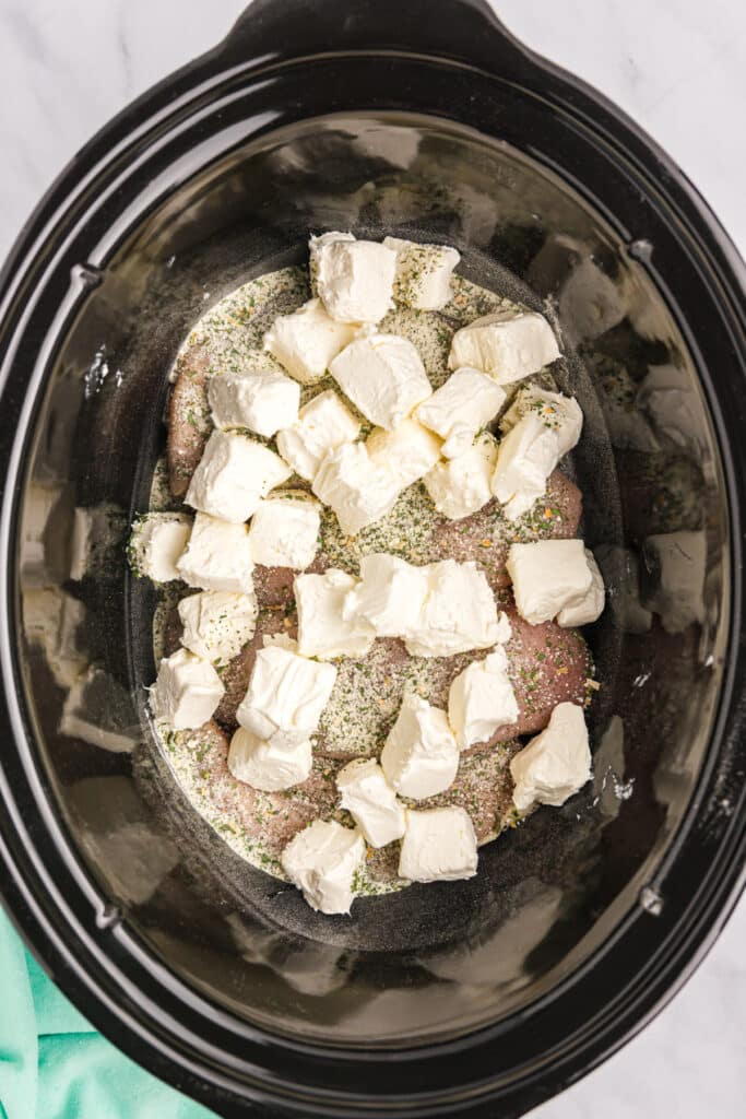 cubed cream cheese on chicken in a slow cooker.