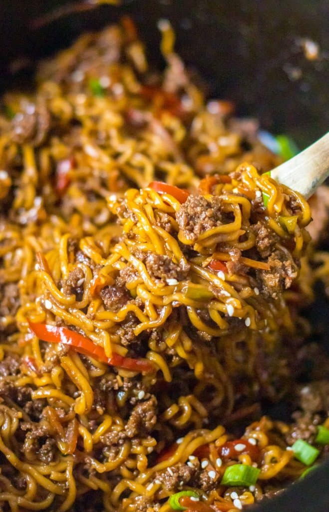 spoon lifting a scoop of beef ramen noodles from a slow cooker.