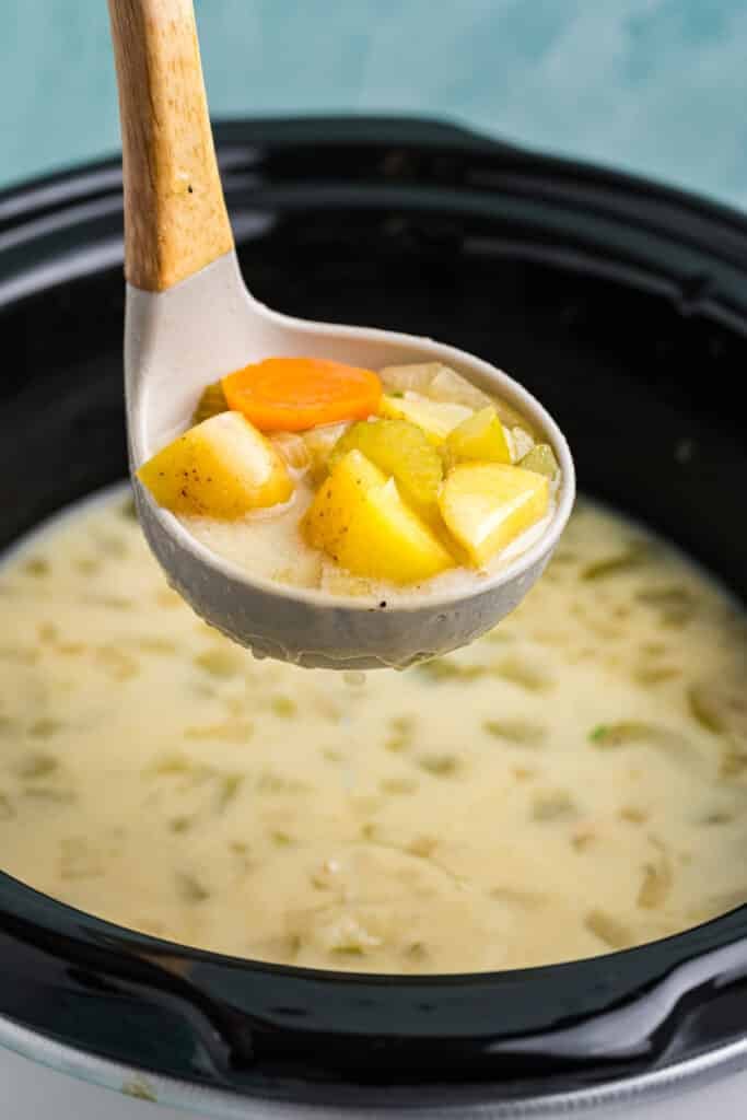 ladle lifting a scoop of dill pickle soup from a slow cooker.