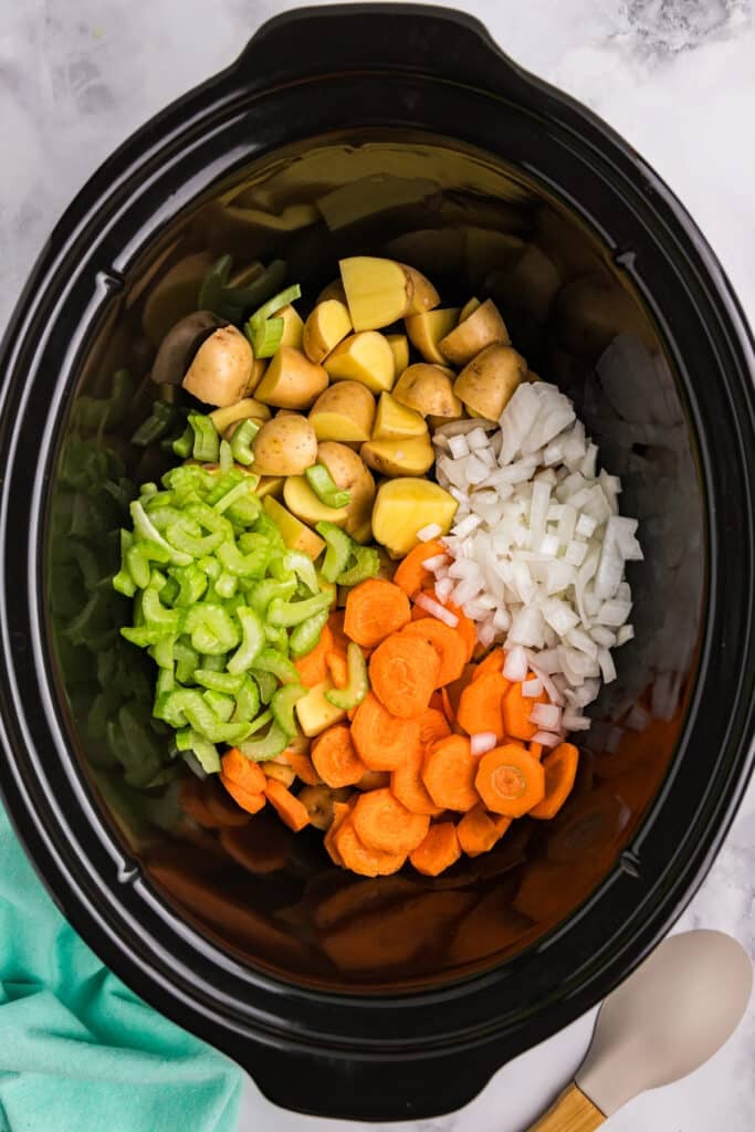 overhead shot of diced carrots, celery, potatoes, and onions in a crockpot.