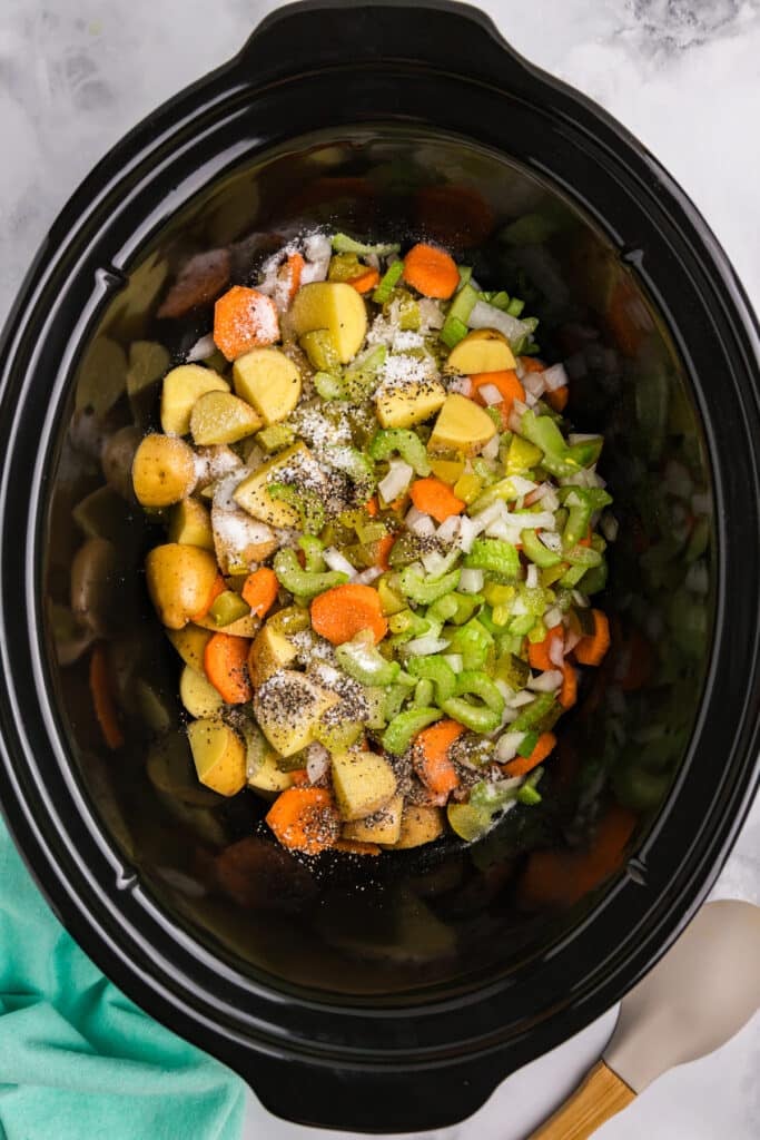overhead shot of diced veggies and seasonings in a crockpot.