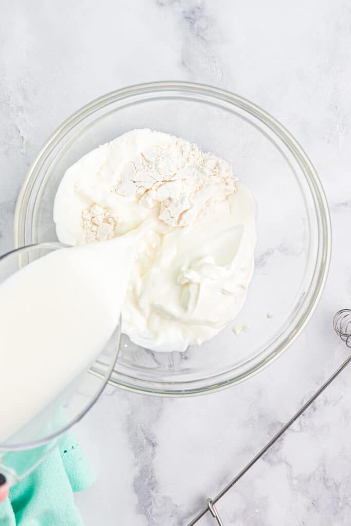 milk pouring into a bowl of flour and sour cream.